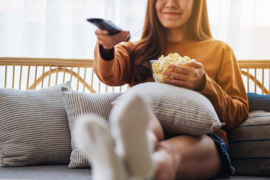 Woman sits on the couch smiling, holding a bowl of popcorn and watching Sasktel max TV